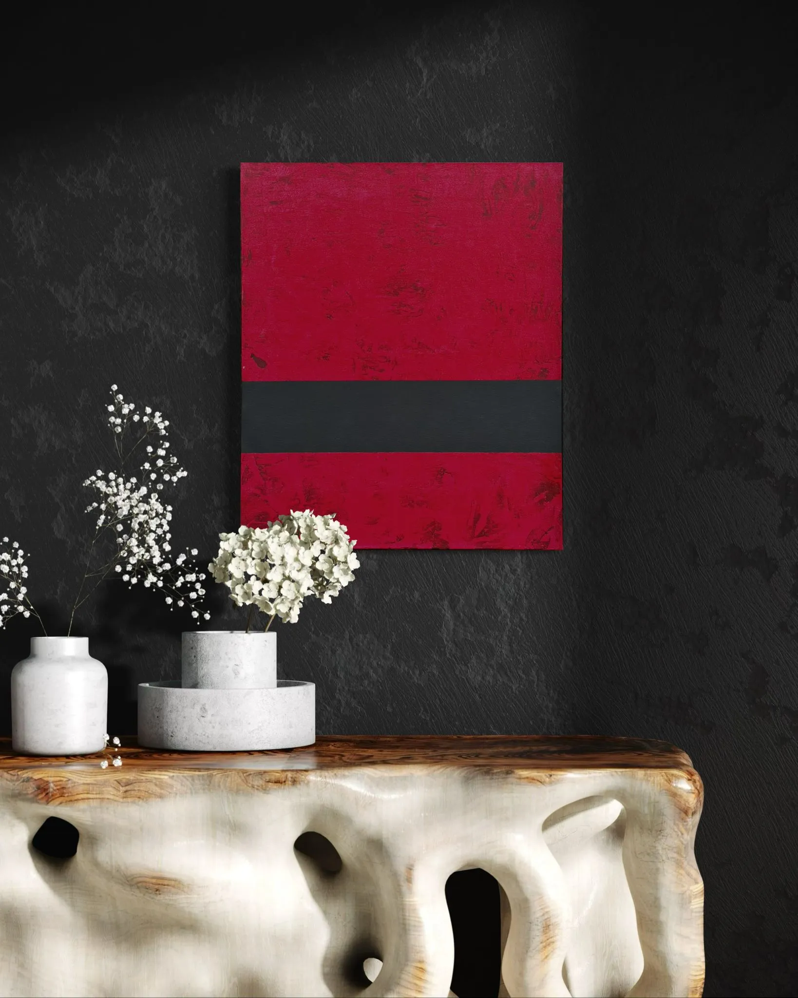 Djupröd tavla med ett grafitgrått band, på en svart vägg ovanför ett skulpturalt trädbord med vita blommor.